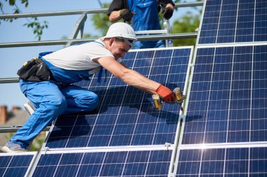 Profesyonel teknisyen tornavida kullanarak metal platforma güneş paneli yükleme. Dış güneş sistemi yükleme, yenilenebilir yeşil enerji üretimi kavramı.