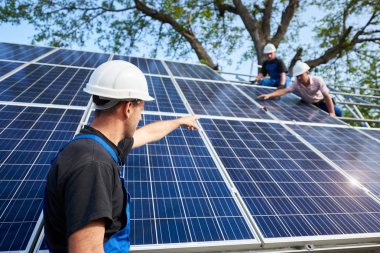 Arkadan görünüşü ile elektrikli tornavida ayakta bitmemiş yüksek dış güneş paneli Fotoğraf volta sistem paneller yüksek çelik platforma bağlayan işçiler işaret önünde teknisyen.