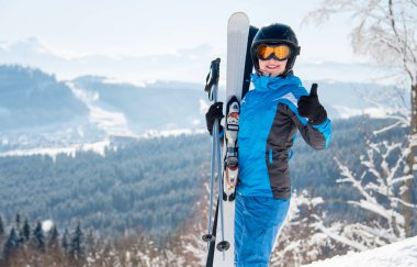 Mavi ski takım, siyah kask ve maske gösteren başparmak yukarı dağlar boşaltmak poz gülümseyen mutlu kadın kayakçı