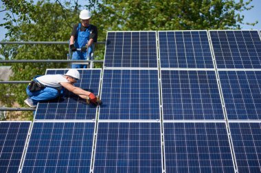 İki teknisyen Elektrikli tornavida metal platform sistemi yeşil parlak güneş Fotoğraf volta paneli bağlanma ile çalışma kalın ağaçlar arka plan ağaç. Yeşil enerji üretim kavramı.