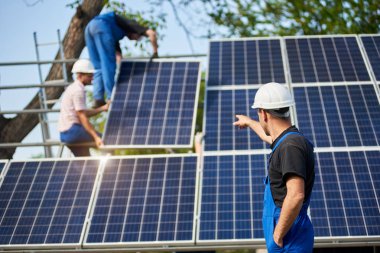 Arkadan görünüşü ile elektrikli tornavida ayakta bitmemiş yüksek dış güneş paneli Fotoğraf volta sistem paneller yüksek çelik platforma bağlayan işçiler işaret önünde teknisyen.