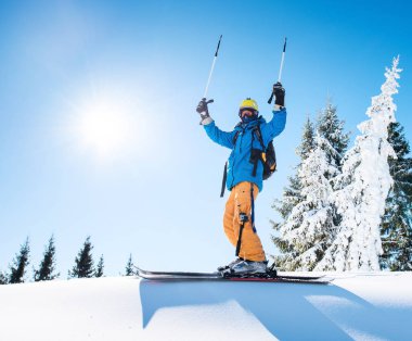 Professional freeride skier holding ski poles raising his arms in the air on the top of the mountain achievement leadership celebration winning happiness positivity gesturing riding lifestyle extreme. clipart