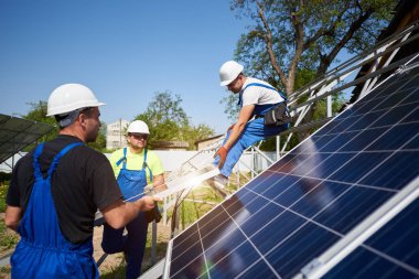 Takım üç profesyonel işçilerin ağır güneş Fotoğraf volta paneller yüksek çelik üzerinde kaldırma. Dış güneş sistemi yükleme, alternatif yenilenebilir yeşil enerji üretimi kavramı.