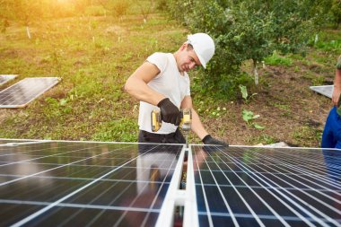 Genç teknisyen tornavida metal platformda dış güneşli yeşil orchard güneş Fotoğraf volta paneli bağlanma ile çalışma ve kırsal arka plan ev sahipliği yapmaktadır. Verimlilik ve profesyonellik anlayışı.