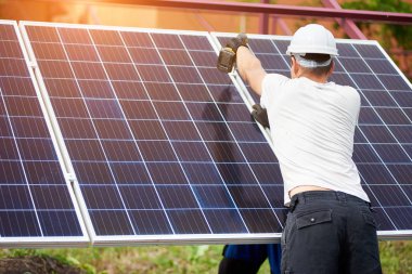 Arkadan görünüşü Genç teknisyen güneş Fotoğraf volta paneli metal platformu üzerinde parlak güneşli yaz gün açık havada Elektrikli tornavida kullanarak bağlanma. Alternatif yenilenebilir enerji üretimi kavramı.