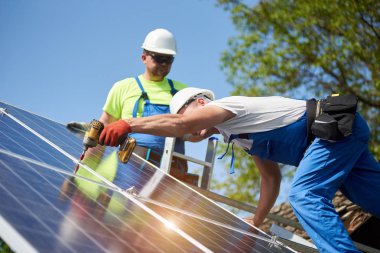 Güneş Fotoğraf volta paneli metal platformu üzerinde parlak mavi gökyüzü tornavida kullanarak bağlanan iki profesyonel teknisyen uzay arka plan kopyalayın. Tek başına dış güneş paneli sistemi kurulması.