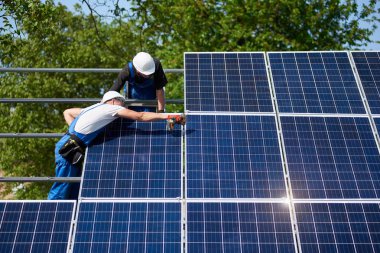 İki teknisyen Elektrikli tornavida metal platformu sistemine yeşil parlak güneş Fotoğraf volta panelinin kurulumu ile çalışma kalın ağaçlar arka plan ağaç. Yeşil enerji üretim kavramı.