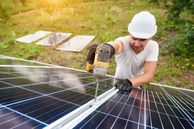 Gülümseyen güneşli yeşil orchard ve kırsal konutlarında arka plan dış metal platformda güneş Fotoğraf volta paneli bağlanma tornavida ile çalışan teknisyeni. Verimlilik ve profesyonellik anlayışı.