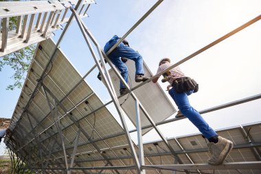 İki mühendis parlak açık mavi gökyüzü arka plan üzerinde uzun boylu çelik platformda ağır panelini takma görünümünden tek başına dış güneş sistemi içinde alt. Ekolojik enerji üretim kavramı.