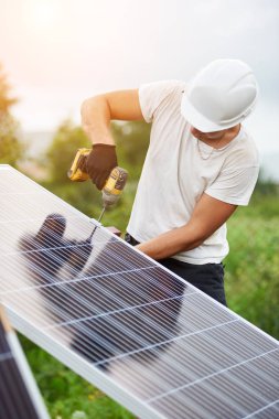 Bağlantı güneş Fotoğraf volta paneli parlak güneşli gökyüzü ve yeşil ağaçlar arka plan Elektrikli tornavida kullanarak platformu için profesyonel işçisi kask ve koruyucu eldiven.