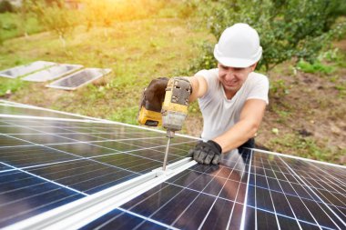 Gülümseyen güneşli yeşil orchard ve kırsal konutlarında arka plan dış metal platformda güneş Fotoğraf volta paneli bağlanma tornavida ile çalışan teknisyeni. Verimlilik ve profesyonellik anlayışı.