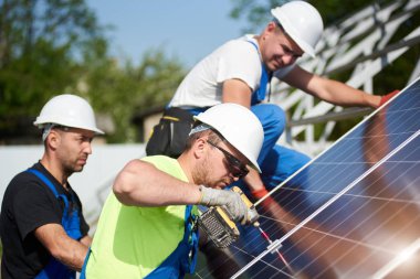 Mavi gökyüzü arka plan üzerinde metal platformu için güneş Fotoğraf volta panelinin kurulumu üç profesyonel teknisyenleri. Tek başına güneş sistemi yükleme, verimlilik ve profesyonellik kavramı.
