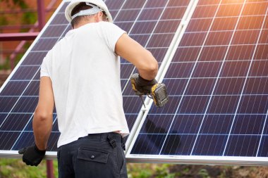 Arkadan görünüşü Genç teknisyen güneş Fotoğraf volta paneli metal platformu üzerinde parlak güneşli yaz gün açık havada Elektrikli tornavida kullanarak bağlanma. Alternatif yenilenebilir enerji üretimi kavramı.