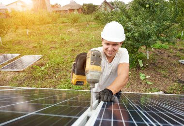 Gülümseyen güneşli yeşil orchard ve kırsal konutlarında arka plan dış metal platformda güneş Fotoğraf volta paneli bağlanma tornavida ile çalışan teknisyeni. Verimlilik ve profesyonellik anlayışı.