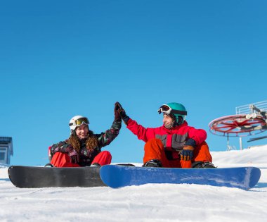 Güneşli bir günde bir yamaç bir mavi gökyüzü ve teleferik kış kayak arka plan üzerinde karşı kar başında otururken bir beşlik birbirlerine vererek snowboard birkaç başvurmak.