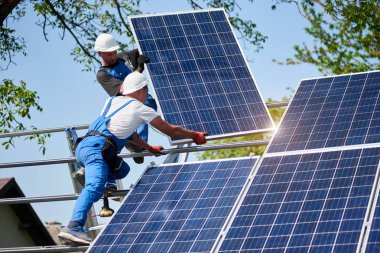 İki işçi yeşil ağaç ve mavi gökyüzü arka plan üzerinde uzun boylu çelik platformda ağır güneş Fotoğraf volta panel montaj. Dış tek başına güneş paneli sistemi kurulması, tehlikeli bir iş kavramı.