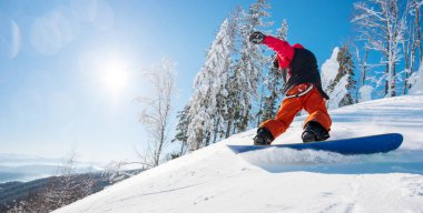 Yatay düşük açılı bir yamaçta güneşli kış gününde dağlarda at binme bir erkek snowboard kadeh. Orman, mavi gökyüzü ve güneş arka planda. boşaltmak freeride snowboard aktif yaşam tarzı