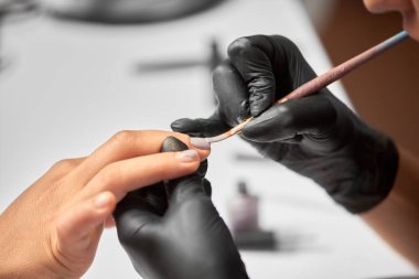 Güzellik salonunda manikür yapma işlemi. Siyah eldiven hafif bulanık kopya alan arka plan üzerinde fırça kullanarak istemci kadın çivi pastel vernik uygulayarak profesyonel güzellik uzmanı Close-up eller.
