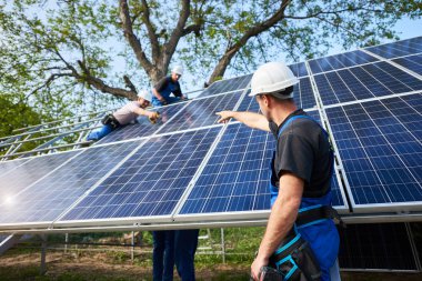 Elektrikli tornavida ayakta önünde tamamlanmamış yüksek dış güneş paneli Fotoğraf volta sistem paneller yüksek çelik platforma bağlayan işçiler işaret ile genç erkek teknisyen.