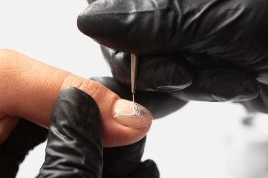 Profesyonel manikürcü Close-up istemci kadın güzellik salonu parlak beyaz zemin üzerine ince aplikatör fırça kullanarak çivi boyalı boyama zarif soyut gümüş glitter desen eller.