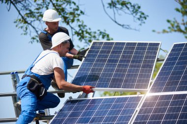 İki işçi mavi gökyüzü arka plan üzerinde uzun boylu çelik platformda ağır güneş Fotoğraf volta panel montaj. Dış tek başına güneş paneli sistemi kurulması, tehlikeli bir iş kavramı.