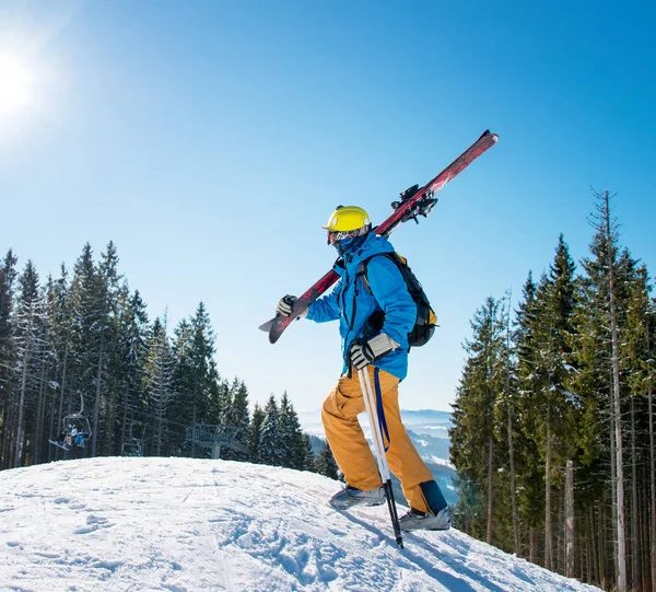 拍摄的男性滑雪者走在山上的斜坡上 在一个阳光明媚的日子 在冬季度假村积极生活方式设备滑雪概念 在他的肩膀上扛着他的齿轮 — 图库照片