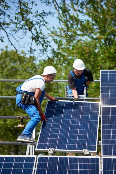 Team of technicians mounting heavy solar photo voltaic panel on tall steel platform on green tree and blue sky background. Exterior solar panel voltaic system installation, dangerous job concept.
