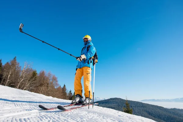 全长枪杀的滑雪者站在一座山在阳光明媚的冬日带相机脚架在冬天度假村 Copyspace 技术回忆自拍照棍子概念上的自拍照 — 图库照片