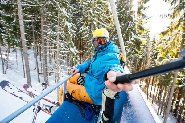 Shot of a skier taking a selfie with a selfie stick while riding ski lift to the top of the mountain at winter sports resort people technology social activity travelling journey trip concept.