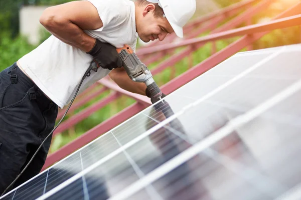 暖かい夏の日に電気ドライバーを使用して金属のプラットフォームに青い光沢のある太陽光発電パネルを接続する技術者のビューをプロファイルします スタンドアロンの太陽電池パネル システム インストールのコンセプト — ストック写真