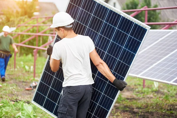 在阳光明媚的夏日温暖的日子里 带着大光泽的太阳光电板的年轻工人的背部观看几乎完成的外部金属平台 可再生生态绿色能源 — 图库照片