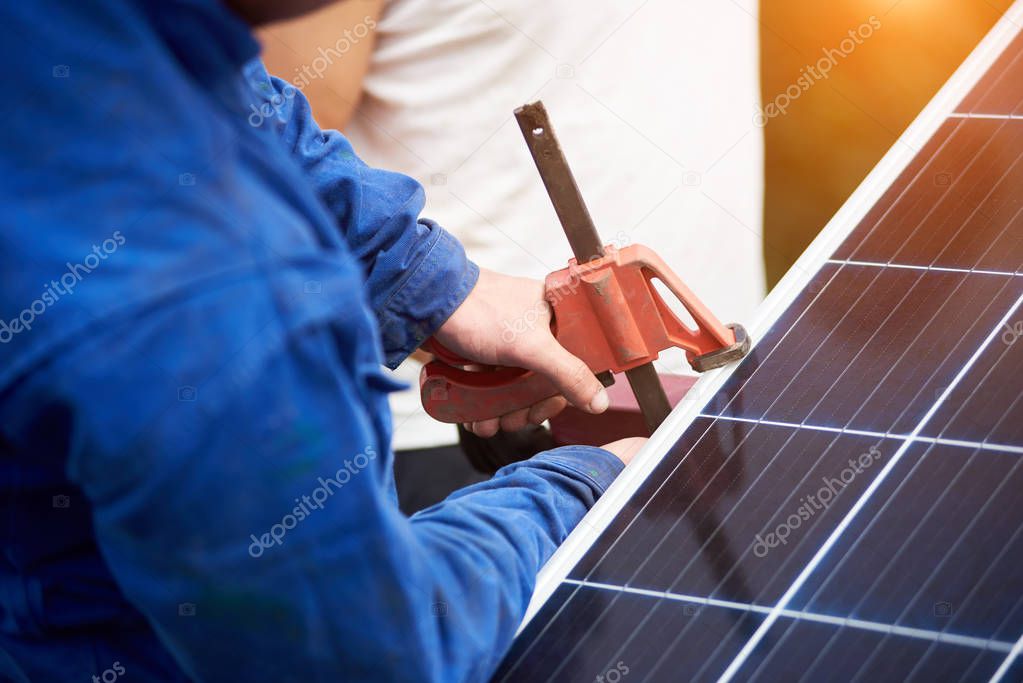 Close-up view of process of connecting solar photo voltaic panel by professional technicians outdoors on bright sunny summer day. Stand-alone exterior solar panel system installation concept.