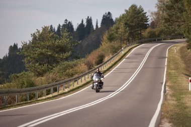 Motosikletçi sisli uzak Yeşil odunsu hills mavi sabah gökyüzü altında arka plan üzerinde parlak güneşli yaz gününde bükülmüş yol boyunca Kruvazör motosiklet Binme siyah deri kıyafet.