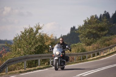 Siyah deri bir kıyafet ve güneş gözlüğü ile Kruvazör motosiklet sürme motosikletçi gülümseyen kollar gergin parlak güneşli yaz gününde