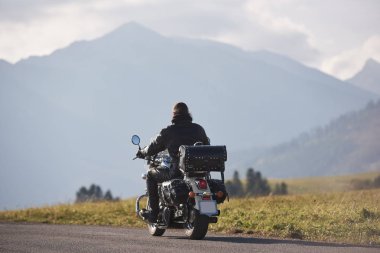Arkadan görünüşü motorcu Road motosiklet sürme güzel sisli odunsu sıradağlarının bulanık kopya alan arka plan üzerinde siyah deri ceketli ve üzerinde parlak güneşli yaz günü bulutlu gökyüzü mavi.