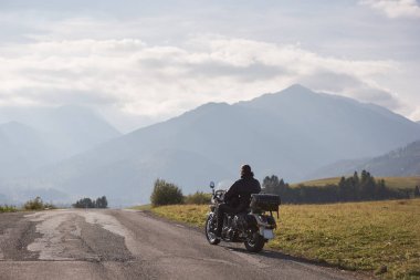 Siyah deri ceketli Kruvazör yol boyunca bulanık kopya alan arka plan güzel sisli Sıradağları ve mavi bulutlu gökyüzü üzerinde parlak güneşli yaz günü Bisiklete binmek motorcycler arkadan görünüm.