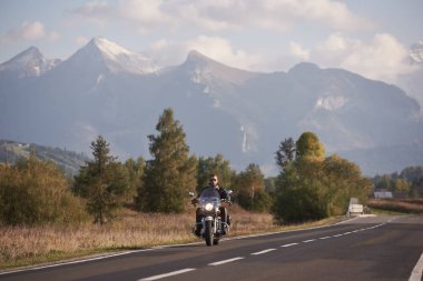Güneş gözlüğü ve siyah deri giyim beyaz karlı zirveleri ve parlak yaz gökyüzü kopya alan arka plan mavi sisli dağlar üzerinde Kruvazör güçlü yüksek hızlı motosiklet sürme sakallı motosikletçi.