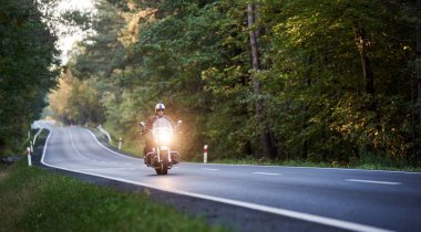 Beyaz kask uzun yeşil ağaçlar arasında güneşli yaz akşamı sarma asfalt yol boyunca motosiklet sürme içinde yakışıklı motorcu