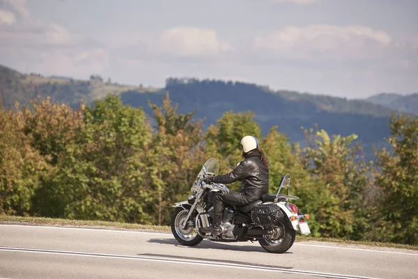 ヘルメット サングラス 黒革の衣類に沿ってクルーザー バイクに乗ってでハンサムなひげを生やしたモーターサイク リストのサイドビューは 日当たりの良い夏の日にアスファルトの道を絞り込む — ストック写真