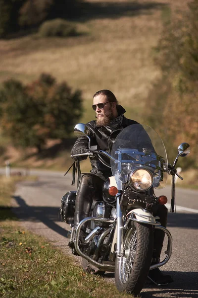 黒革のジャケットとサングラス国道端の巡洋艦のバイクに座っているハンサムなひげを生やしたバイク — ストック写真