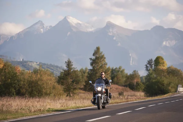 Güneş gözlüğü ve siyah deri giyim beyaz karlı zirveleri ve yaz gökyüzü kopya alan arka plan mavi sisli dağlar üzerinde Kruvazör yüksek hızlı motosiklet sürme sakallı motosikletçi.