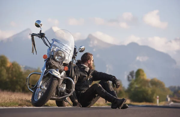 明るい青空の下で遠くの山ピークの領域の背景のぼやけたコピーの沿道に巡洋艦強力な光沢のあるバイクに座って黒い革の衣類でハンサムなモーターサイク リスト — ストック写真