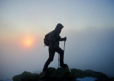 Sırt çantası ve trekking sopalarla sisli bulutlar backgrond üzerinde kayalık dağ tepe üzerinde turist uzun yürüyüşe çıkan kimse adam silüeti