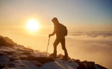 Sırt çantası ve gün batımı arka plan üzerinde kayalık dağ tepe üzerinde dinlenme sopalarla yürüyüş ile turizm uzun yürüyüşe çıkan kimse, arkadan görünüm 