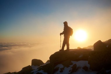 Sırt çantası ve gün batımı arka plan üzerinde kayalık dağ tepe üzerinde dinlenme sopalarla yürüyüş ile turizm uzun yürüyüşe çıkan kimse, arkadan görünüm 