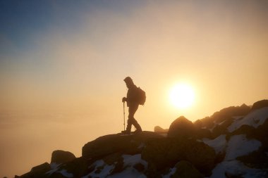 Sırt çantası ve gün batımı arka plan üzerinde kayalık dağ tepe üzerinde dinlenme sopalarla yürüyüş ile turizm uzun yürüyüşe çıkan kimse, arkadan görünüm 