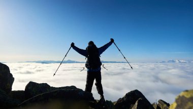 Sırt çantalı turist yürüyüşçüleri ve yürüyüş sopalarıyla kollarını kaldırmış büyük kayalıklarda dikilirken. 