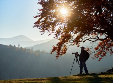 Tripod ve profesyonel fotoğraf makinesi ve dağlar panorama resmini alarak günbatımı arka plan üzerinde kullanarak turist fotoğrafçı silüeti