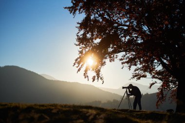 Tripod ve profesyonel fotoğraf makinesi ve dağlar panorama resmini alarak günbatımı arka plan üzerinde kullanarak turist fotoğrafçı silüeti