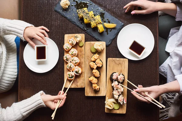 top view of friends eating in oriental restaurant, enjoying sushi set with soy sauce, wasabi and marinated ginger.